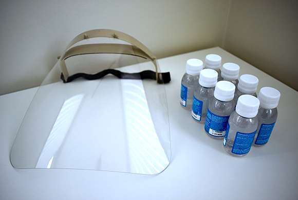 Kit com álcool gel de 60 ml e máscara protetora facial (faceshield) em cima de uma mesa